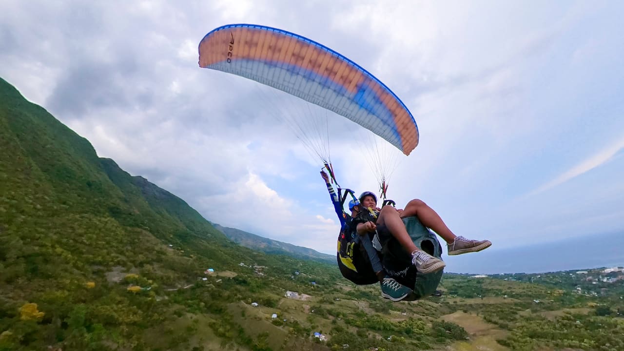 Tandem paragliders soaring over the hills and coastline of Oslob